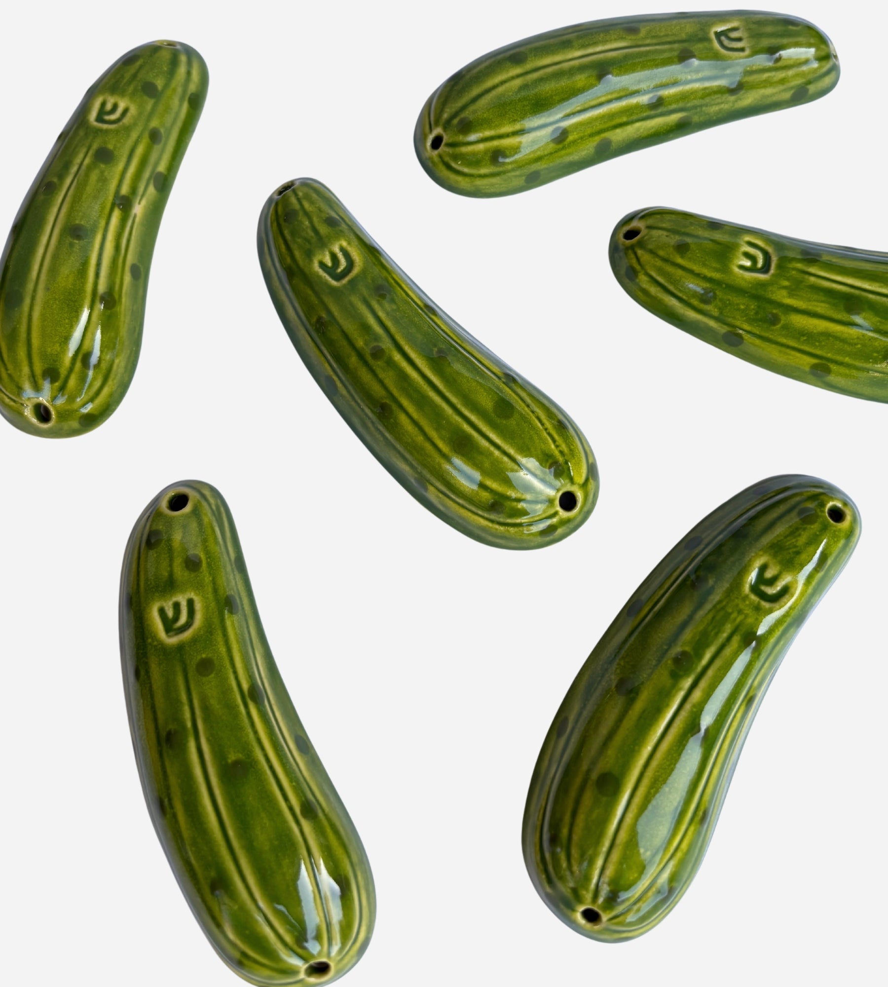 A collection of handmade green pickle mezuzot with installation holes for outdoor doors